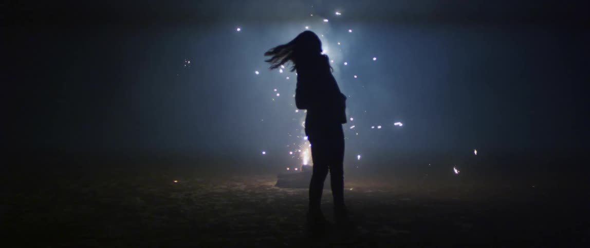 Silhouette of a woman standing in front of a fireworks display at night