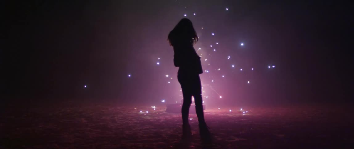 A woman stands outside in front of sparks flying in the air