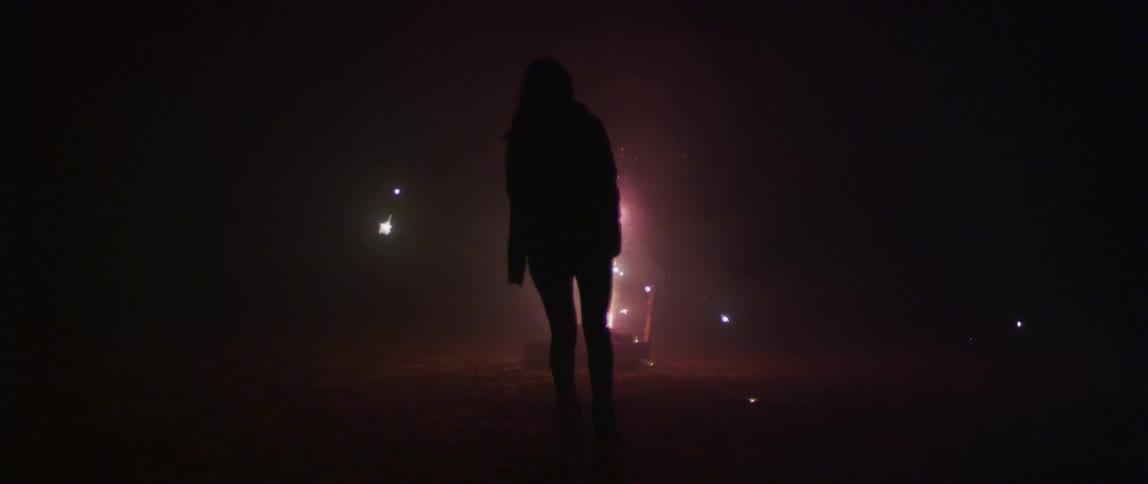 A standing woman is silhouetted by fireworks at night