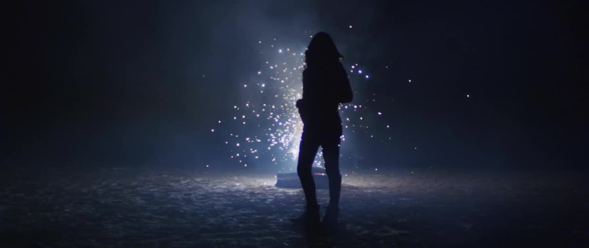 A woman stands in front of sparks flying outdoors at night