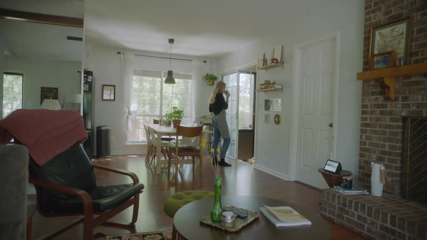A woman drinks from a coffee mug while standing leisurely in a house during the day