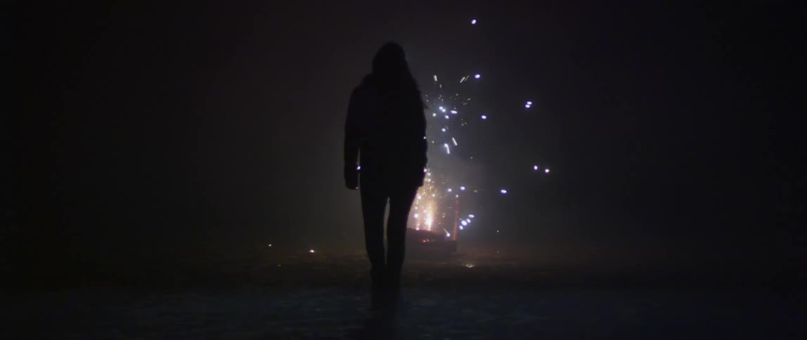 The silhouette of a woman walking towards sparking fireworks at night