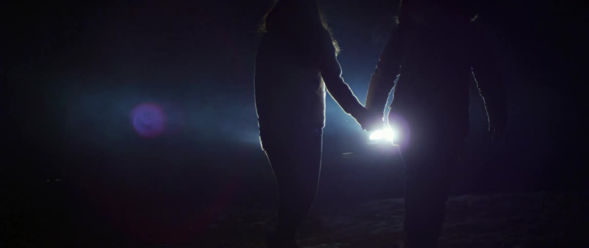 Two people are walking outdoors by a car at night