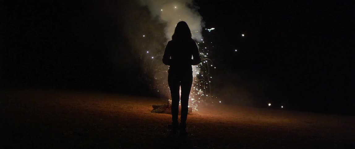 Silhouette of a woman standing in front of a white sparkler firework at nighttime