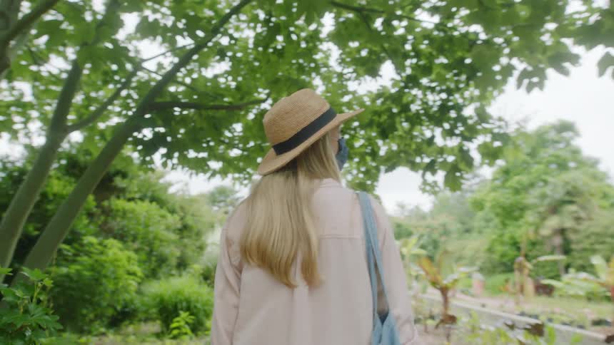 Woman wearing a face mask walks down a narrow brick trail at daytime next to green vegetation