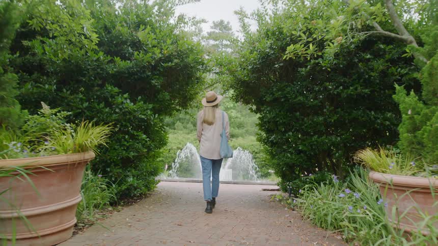A woman walks leisurely along a walkway towards a fountain during the day