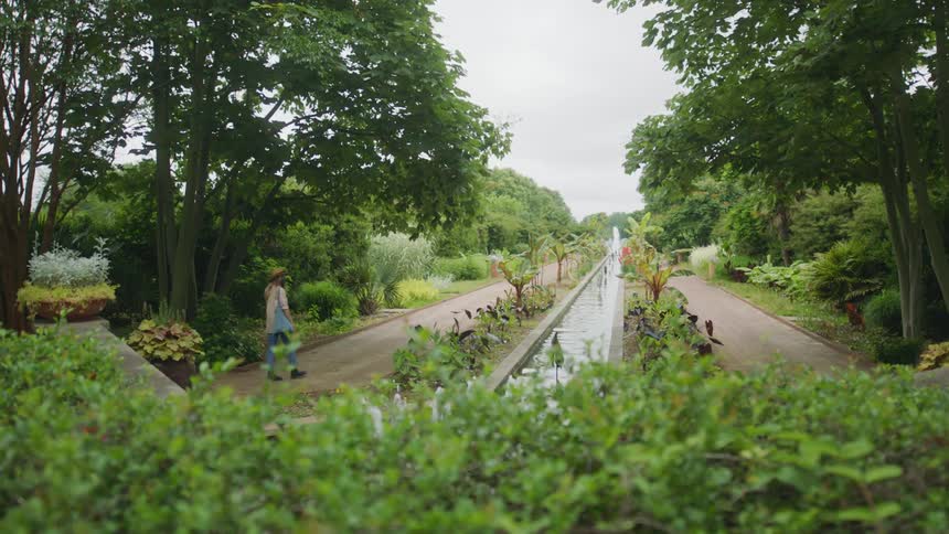 Woman walking through a garden with a water fountain in the middle at daytime