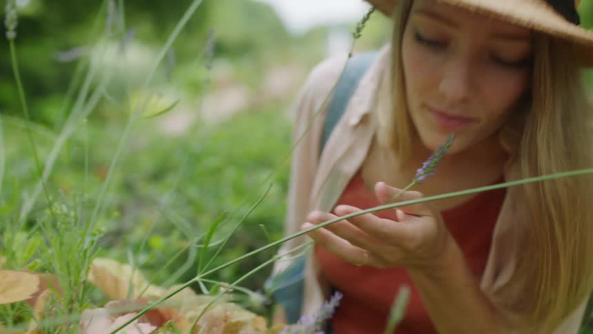 Woman stands in garden smelling flowers growing on stalks