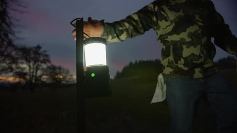 A man with a hat walking up and taking a lantern from a post with the sky and clouds in the background