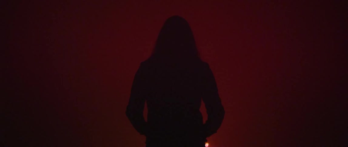 Silhouette of a hooded figure standing in front of red fireworks on a dark environment
