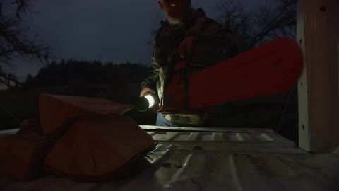 Man places a chainsaw on the bed of a truck while turning off a lamp in a rural area