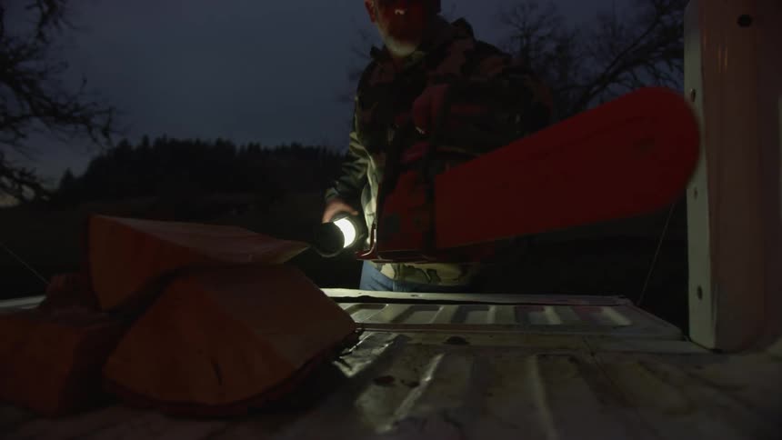 Man places a chainsaw on the bed of a truck while turning off a lamp in a rural area