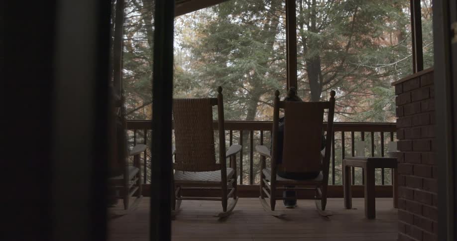 A person sitting in a wooden rocking chair in the porch of a cabin in the woods
