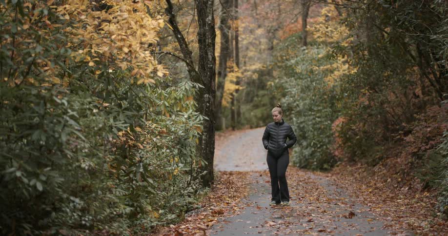 A woman is walking on a forest path covered with leaves in the fall