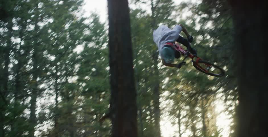 Cyclist jumps a dirt ramp with a mountain bicycle in the forest at sunset