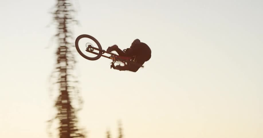 A teenager on a bicycle rides over a dirt mound in a forest and turns in the air