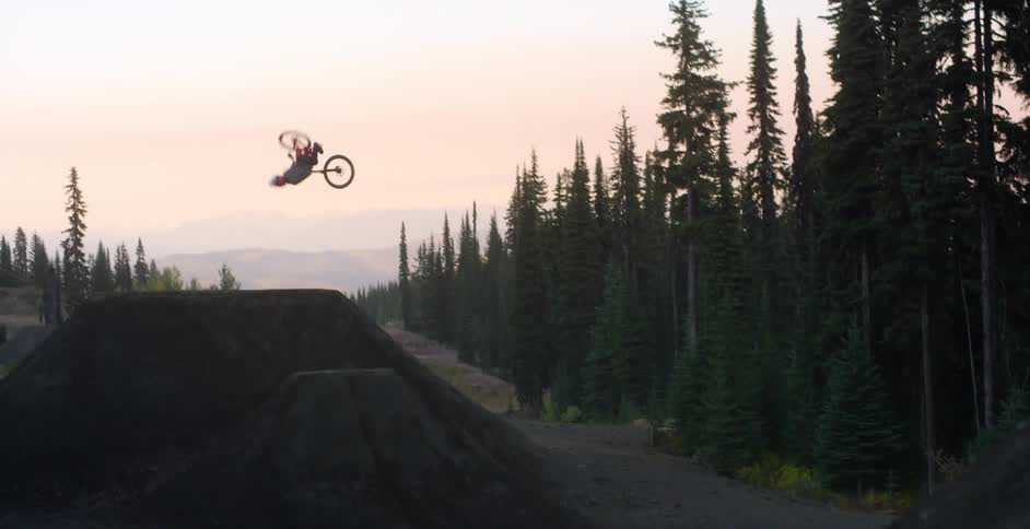 A person riding a bmx bike flips over a large jump in a forest