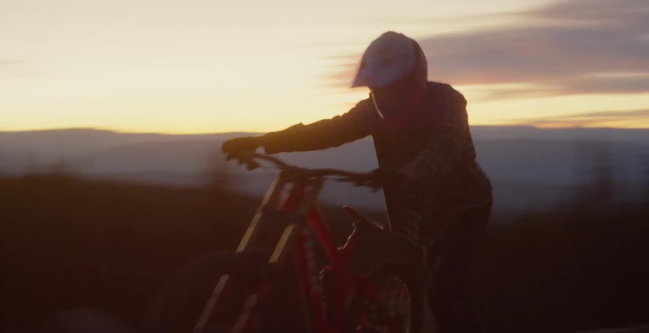 Man pushes a mountain cross country bicycle on top of a mountain at sunset