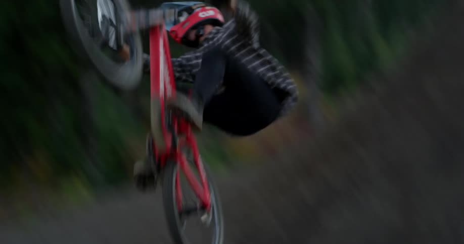 Cyclist riding a mountain bicycle over a dirt ramp near the forest at sunset