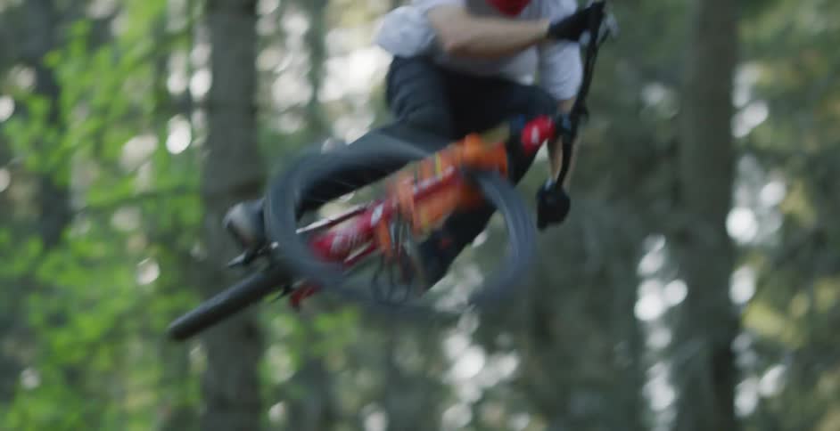 A man on a bicycle leaps in the air as he rides over a hill on a trail in the forest