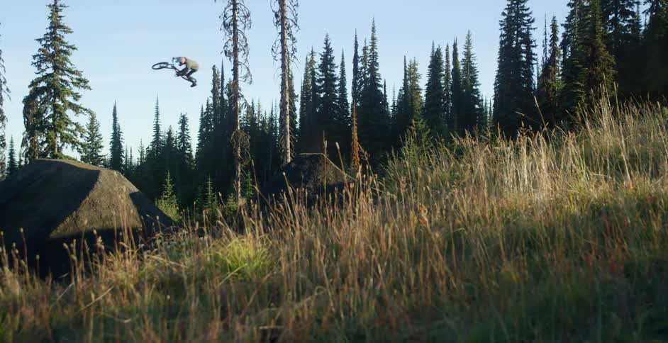 A person with a helmet riding a bike on an obstacle course in the woods and doing tricks