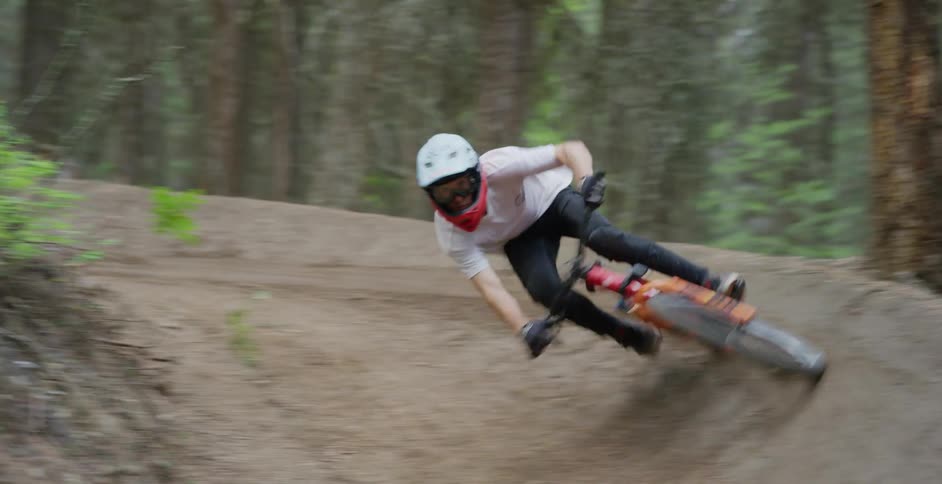 A boy rides a mountain bike quickly around a curve on a dirt road in a forest