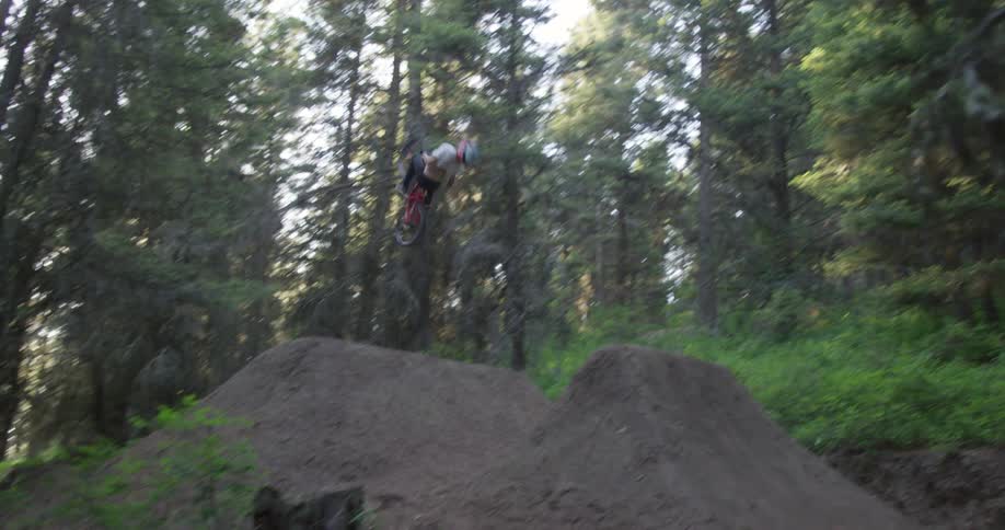 A person with a helmet riding a bike on an obstacle course in the woods and doing tricks