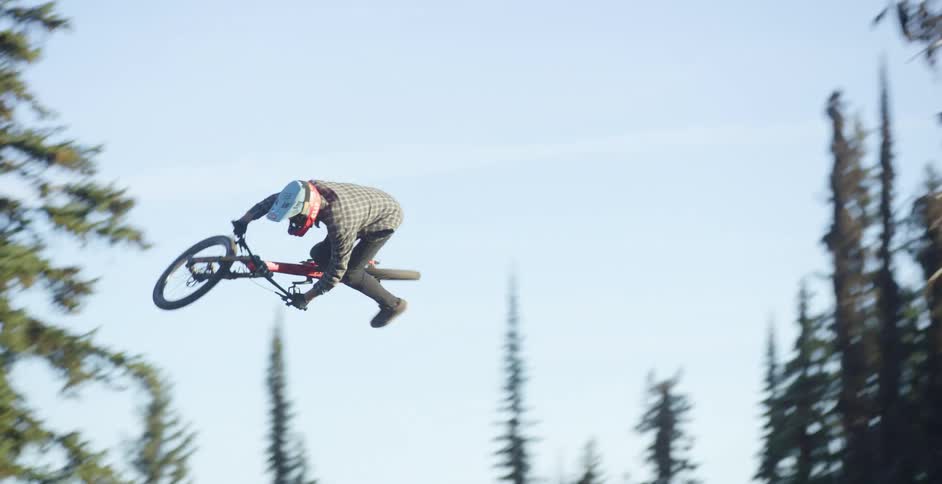 A cyclist becomes airborne after riding a bicycle up a dirt ramp before flying over a taller ramp and safely landing on its slope