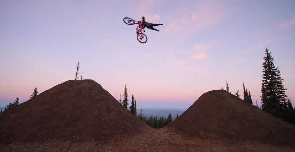 A person on a mountain bike goes over a hill and jumps on their bike