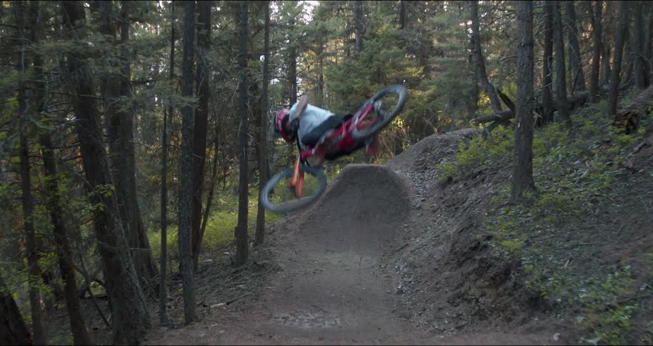 A person with a helmet riding a bike on an obstacle course in the woods and doing tricks