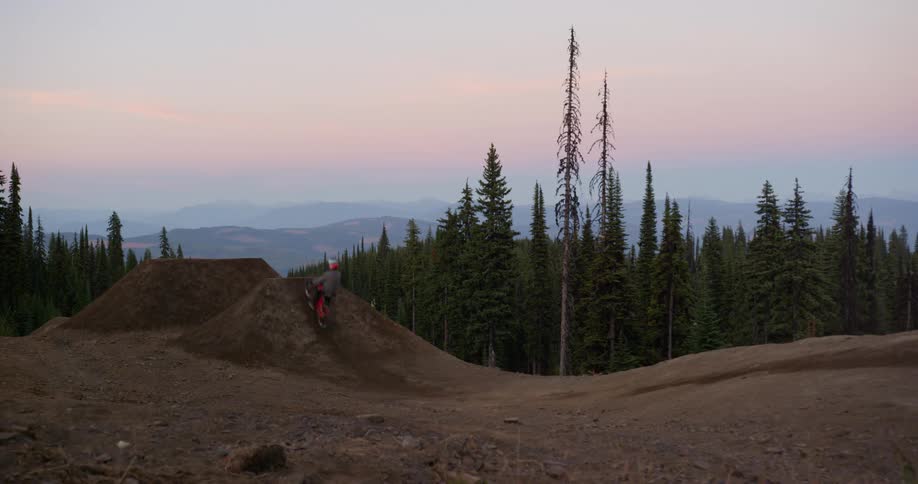 Man on a mountain bike performing a jump over a dirt slope in the evening time