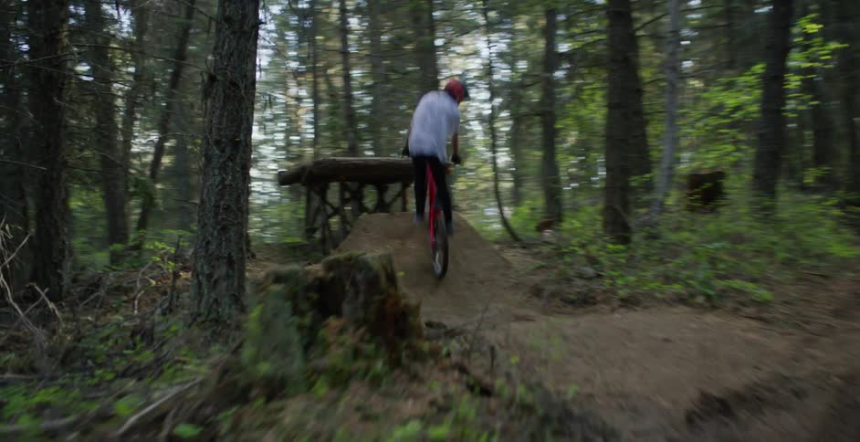 Cyclist rides a bicycle over the ramps of a dirt track through the forest