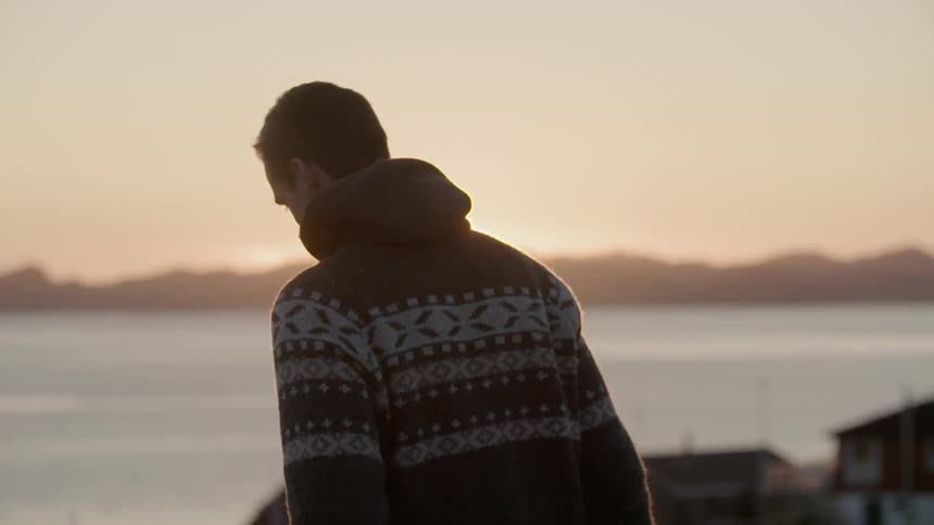 A man walks toward the ocean at sunset