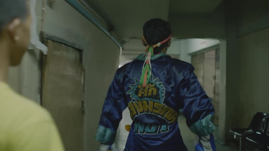 A muay thai fighter does stretches while walking through a corridor before a fight