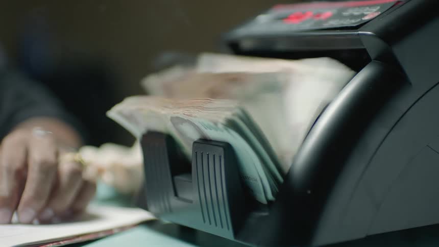 A hand starts a bill counting machine while cigarette smoke wafts up from the side