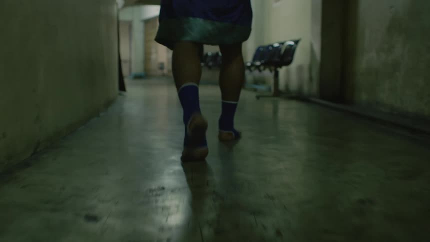 A man with socks and a robe walking down a hallway with chairs