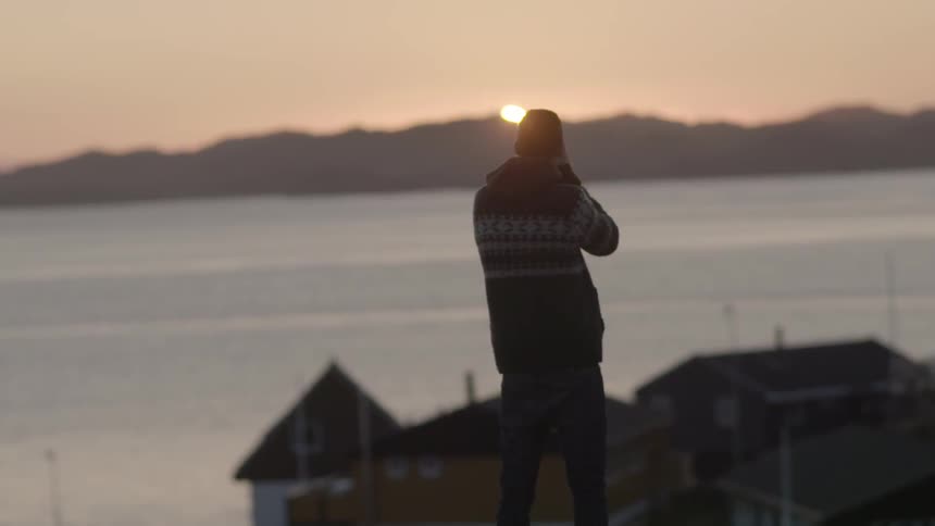A person is photographing the sun setting in the distance