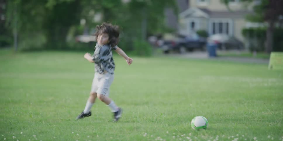A young boy runs and kicks a soccer ball by himself in a large open grass field