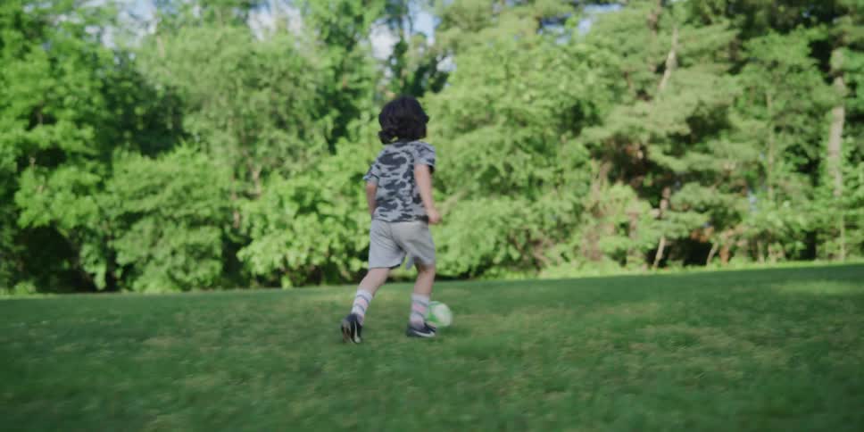 Two youngsters are playing with a soccer ball in a large grassy field
