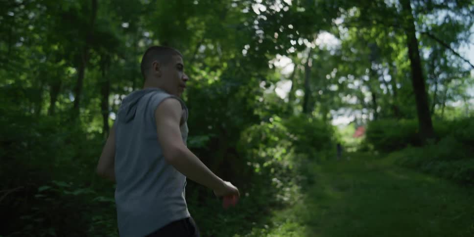Teenage boy walking on a grass pathway in a green forest at daytime