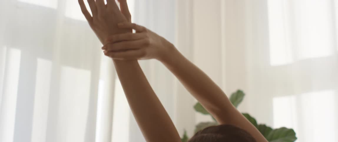 A young woman does stretches in front of a window in a house during the day