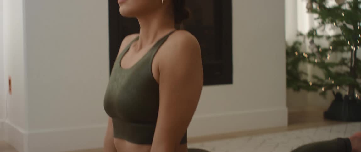 A young woman does yoga on a mat in the living room of a house during the day