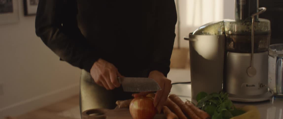 A young woman uses a knife to cut a fruit on a wooden cutting board in the kitchen of a house during the day