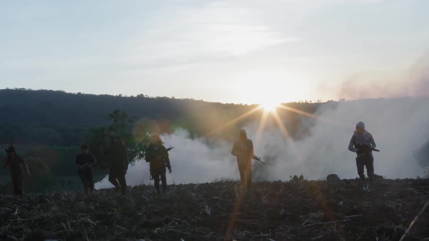 A group of people carrying guns walk in front of smoke