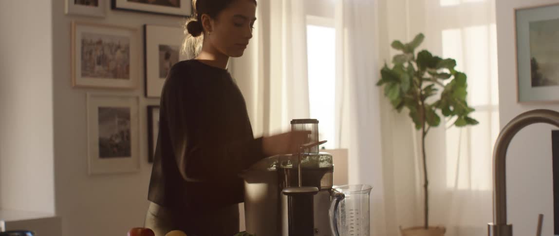 A woman places a slice of fruit in an electric fruit juicer and presses down on the lid to produce juice