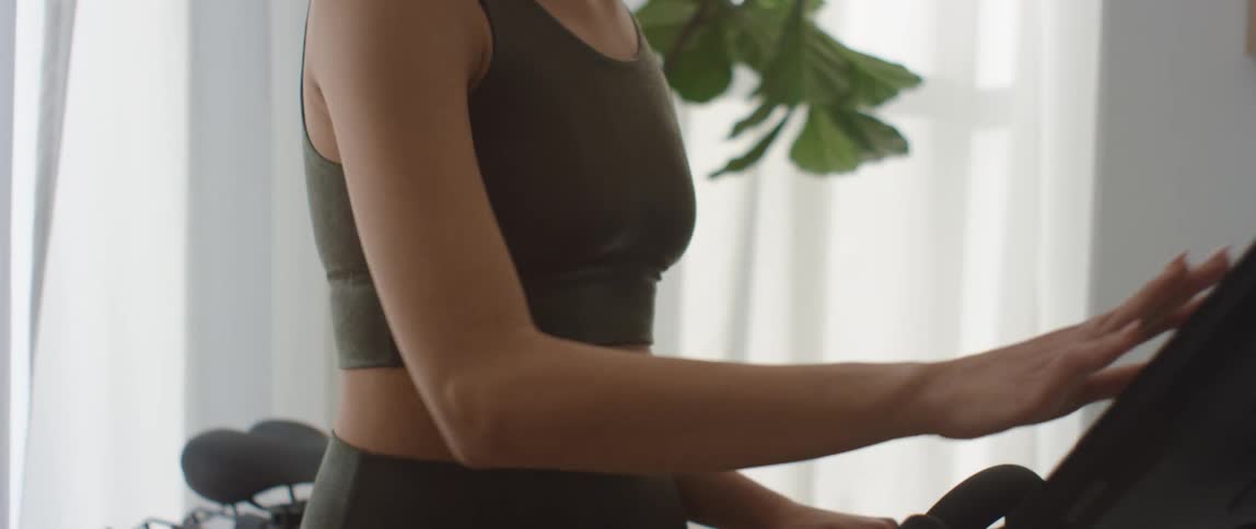 A woman gets ready to use an indoor exercise bike and scrolls through the attached monitor