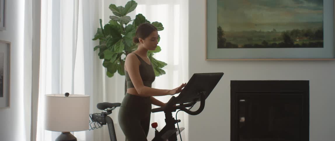 Young fit woman wearing sports clothes programs a stationary exercise bike