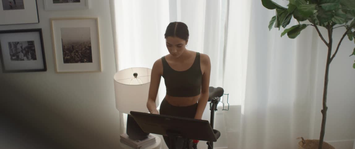 Young fit woman wearing exercise clothing adjusts a stationary workout bike at home
