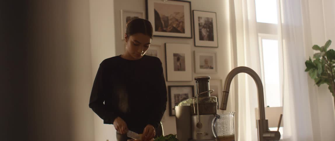 A woman at home cuts vegetables and puts them in a juicer