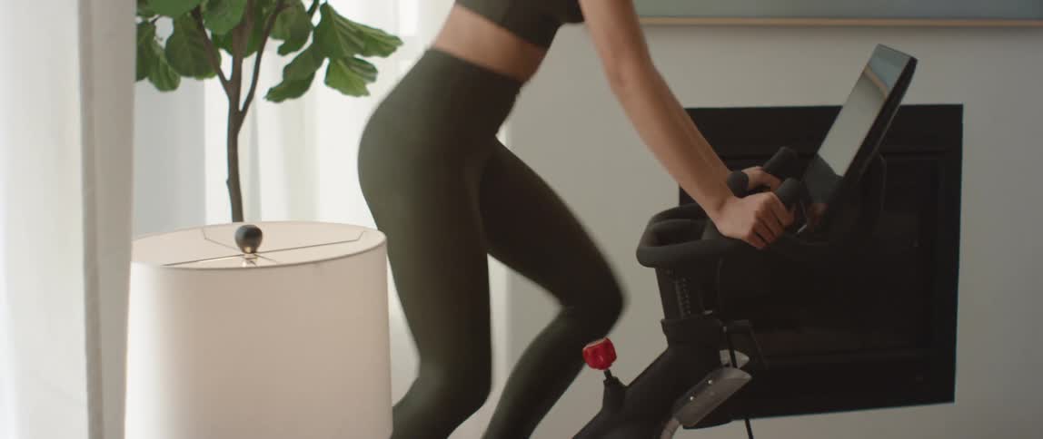 Young fit woman in sports clothes exercises on a static cycle at home